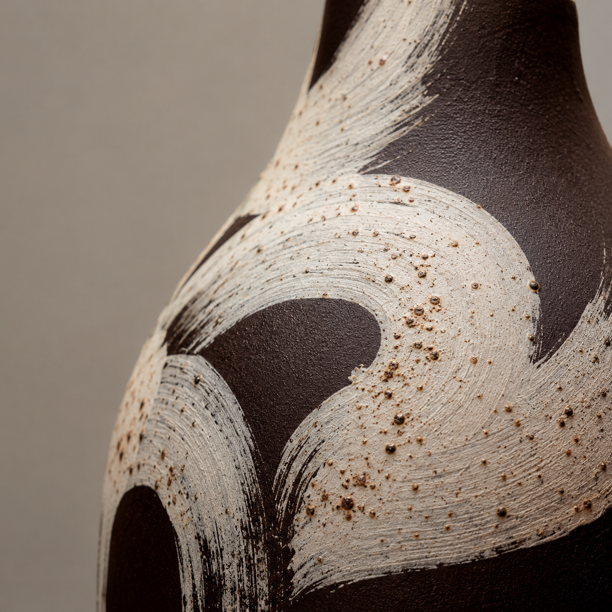 Close-up of a ceramic vase with textured surface and brown speckles on a neutral background